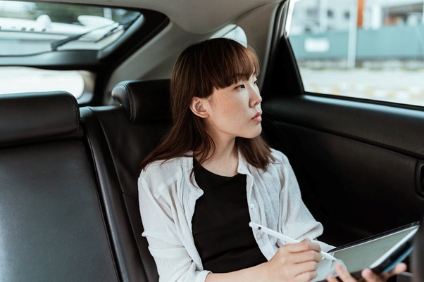 A woman using a tablet inside a taxi.