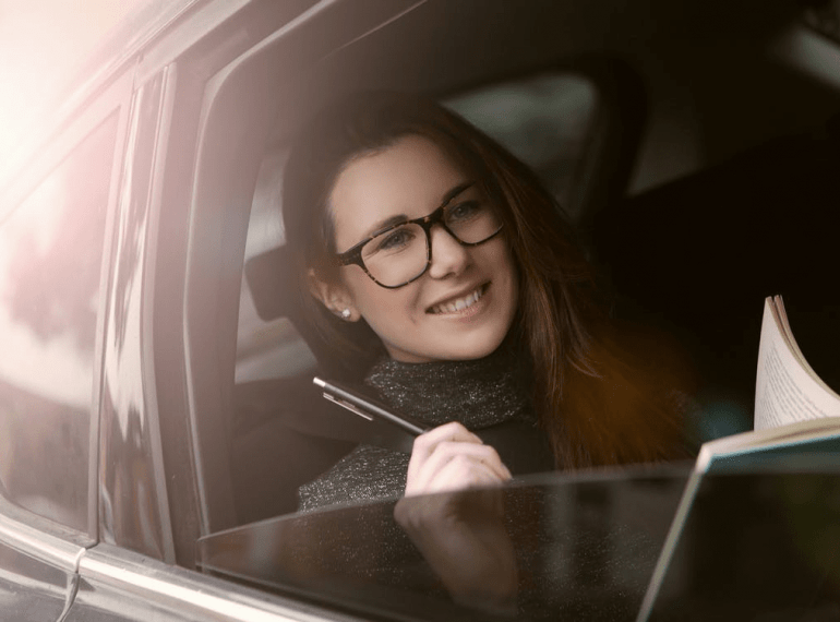 A woman is travelling in a taxi with a pen and notebook
