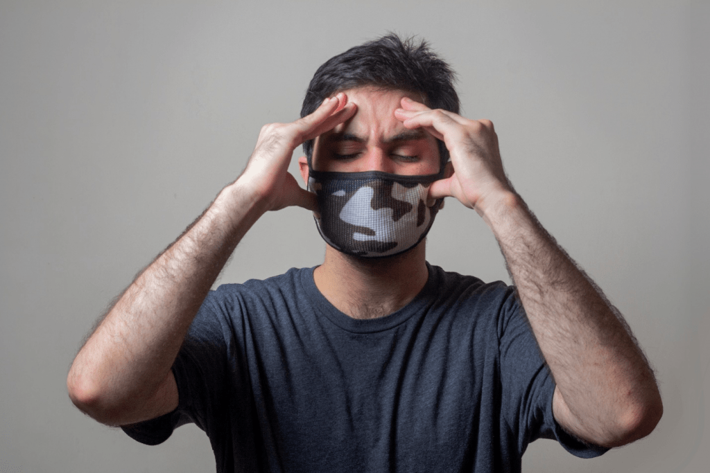 a man in a grey shirt wearing a mask and holding his head