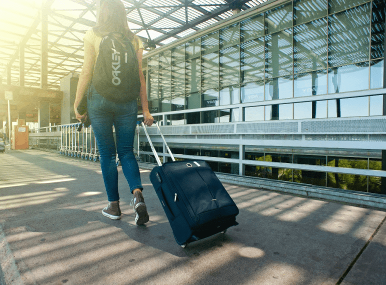 a woman wearing a backpack walking on a pathway while strolling her luggage