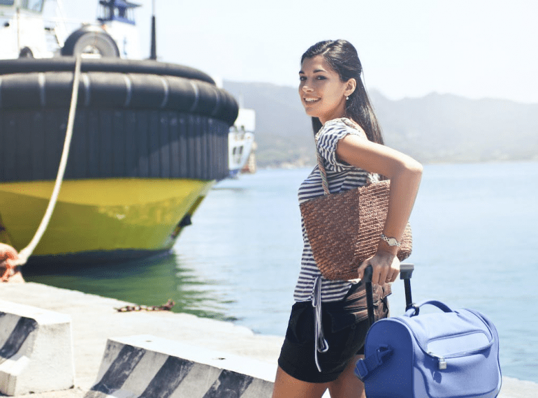 Woman standing on the dock near the ship holding luggage and carrying a handbag