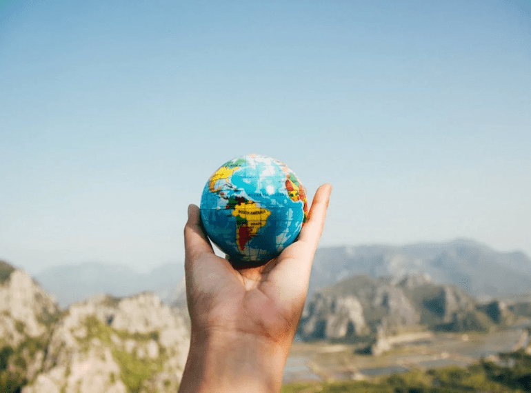 An image of a person holding a mini globe in their hand while facing the mountains