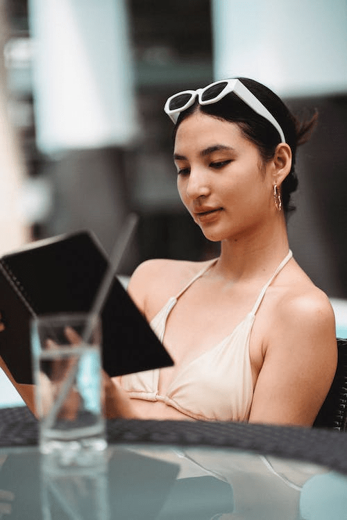 An image of a serious young ethnic woman reading notes in her planning while relaxing at a poolside during the summer