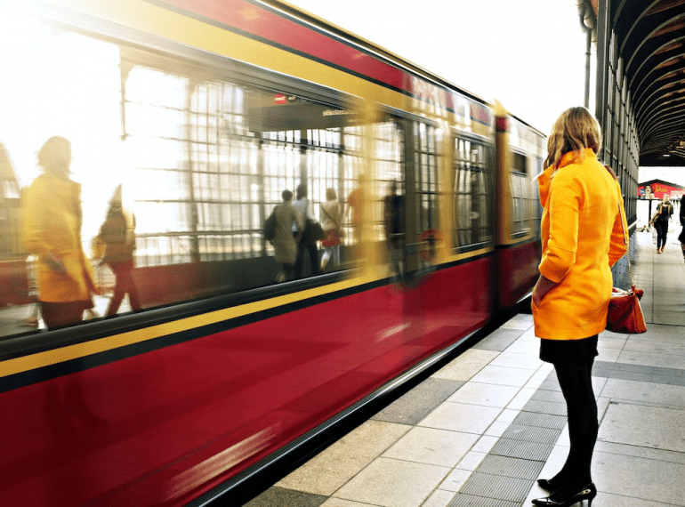 An image of a woman wearing a yellow coat standing on the subway station beside red train