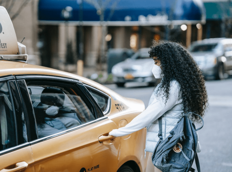 An image of an anonymous ethnic female passenger opening the door of a taxi on the street