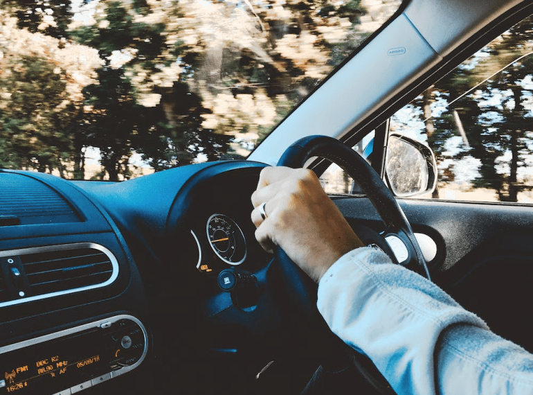 An image of a person holding a black steering wheel in a car