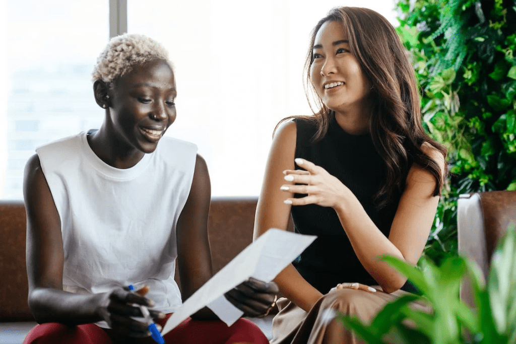 An image of a two cheerful female colleagues talking about important documents