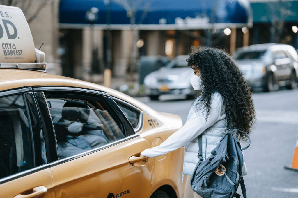 An image of an anonymous ethnic female passenger opening the door of the taxi on the street