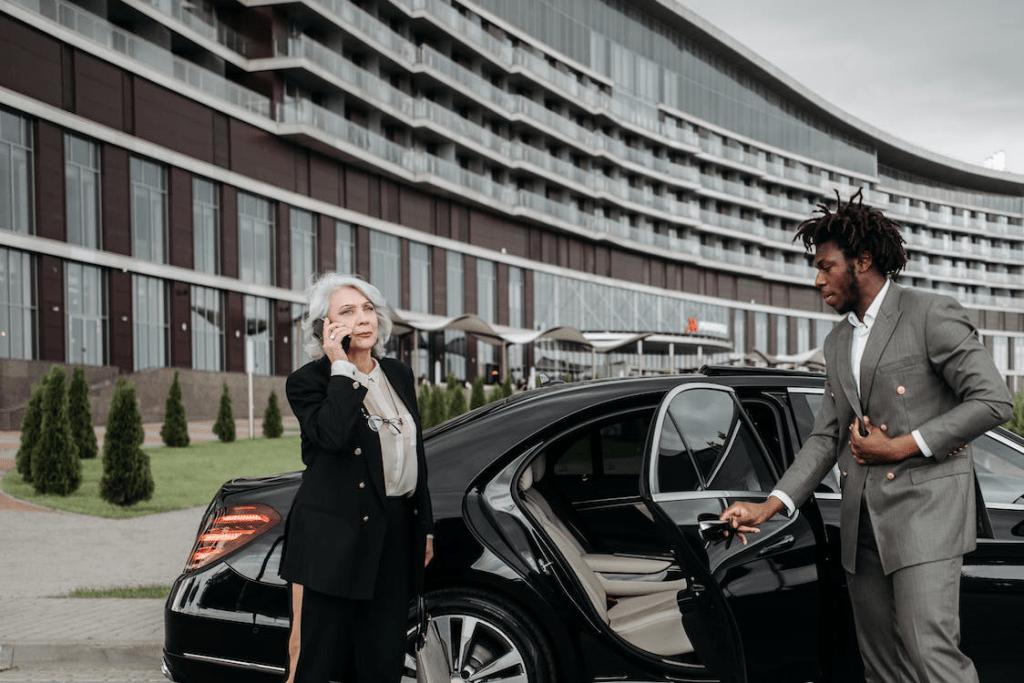 An image of a man in grey suit opening the car door for a woman in a black suit