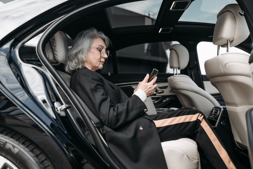 An image of a woman wearing a black coat while holding her phone and sitting inside a car