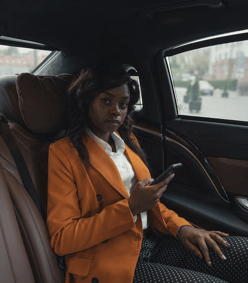 An image of a woman wearing an orange blazer and holding her phone while sitting in a car