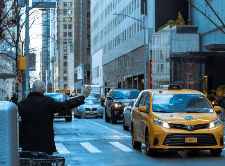 An image of a man wearing a black coat while standing on the side of the street and waiting for a taxi