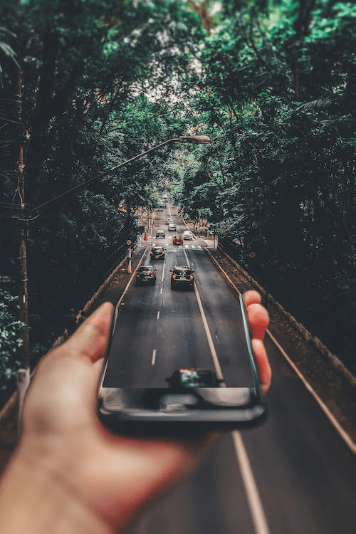 Forced perspective photography of cars running on a road below a smartphone in a person’s hand