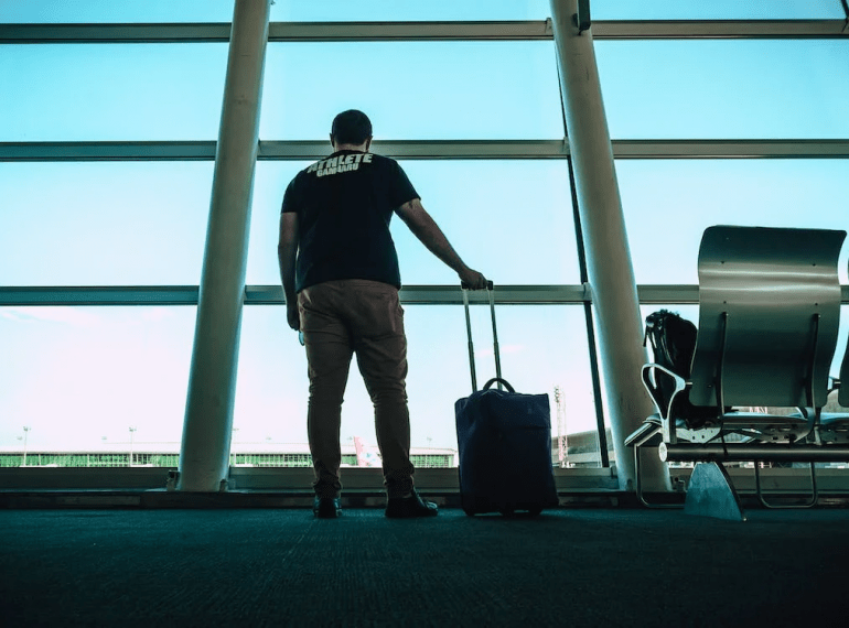 An image of a man holding a bag and standing facing a huge window inside an airport