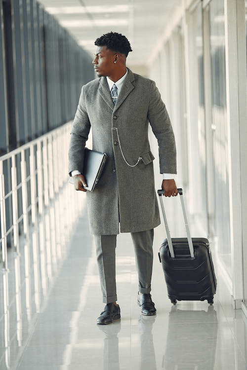 An image of a man wearing a grey coat and carrying his suitcase