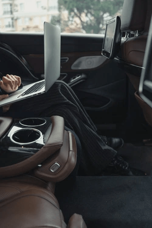 An image of a person using a laptop in the backseat of a luxurious car