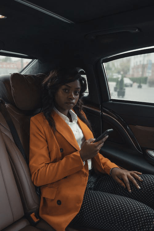 An image of a woman wearing an orange blazer and holding her phone while sitting in a car